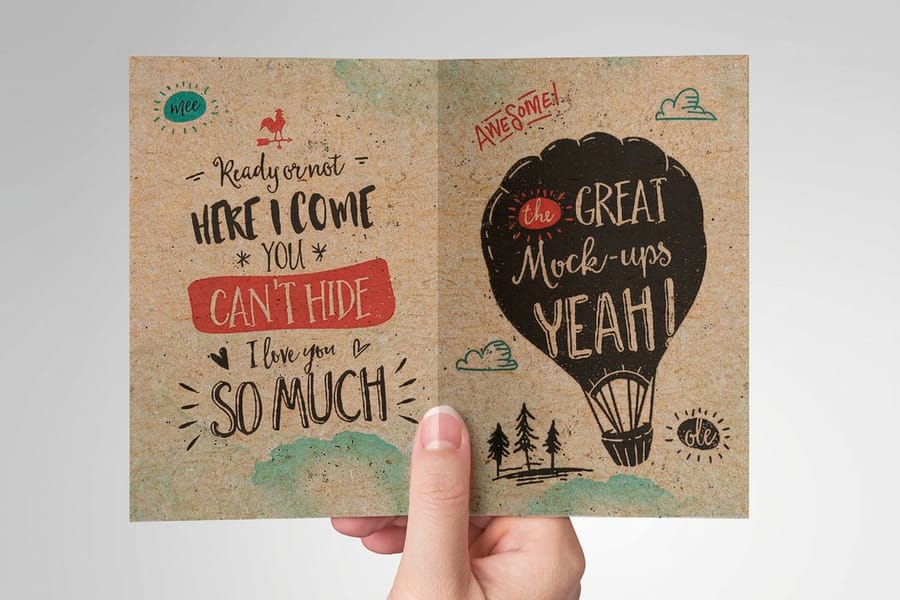 A kraft greeting card with a hand drawn hot air balloon design printed by 4OVER4, held open in one hand